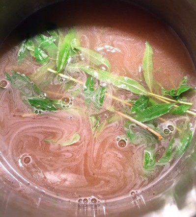 Whole branches of lemon verbena in the liquid as it comes to the boil.